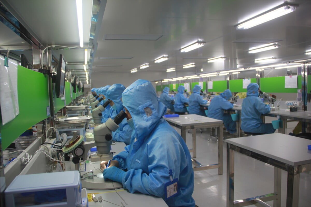 Arbeiter in einer Fabrik in Schutzkleidung. Sie schauen durch Mikroskope.
