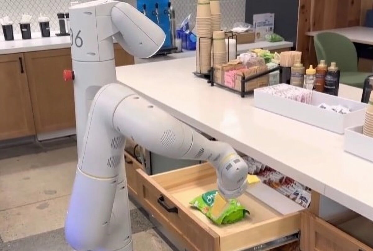 Ein Roboter auf Rädern mit einem Roboterarm greift in eine Küchenschublade und holt eine Tüte Chips heraus.