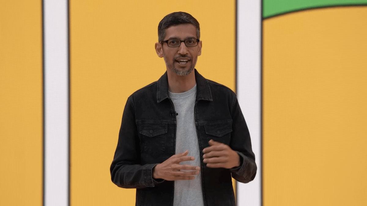 Google CEO vor einer gelben Videoleinwand bei einem Vortrag, spricht in die Kamera.
