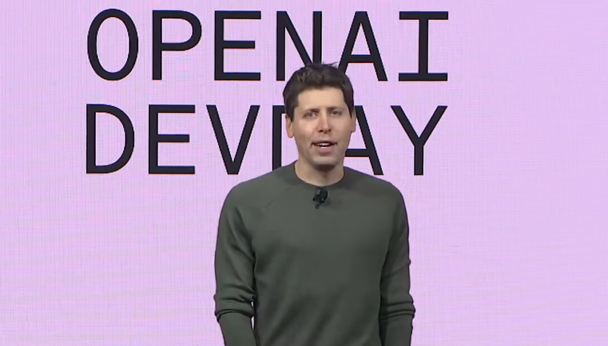 Sam Altman steht auf einer Bühne, hinter ihm ein rosa LCD-Bildschirm mit der Aufschrift "OpenAI Devday".